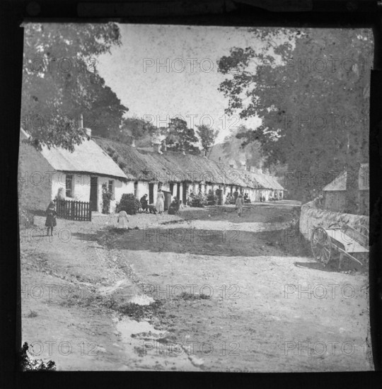 Prosperous looking people sitting outside thatched workers' one storey whitewashed cottages, possibly tourists to the Lake District, England, UK late 1800s c 1900
