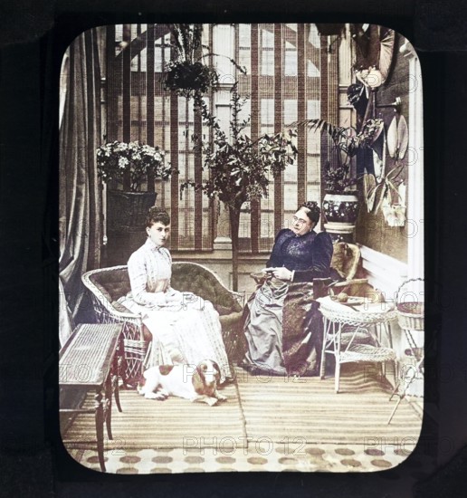 A colourised magic lantern slide of Queen Mary, when Princess May of Teck, with her mother, the Duchess of Teck, formerly Princess Mary of Cambridge, indoors in conservatory room, Victorian period, Britain, UK c 1890-1900