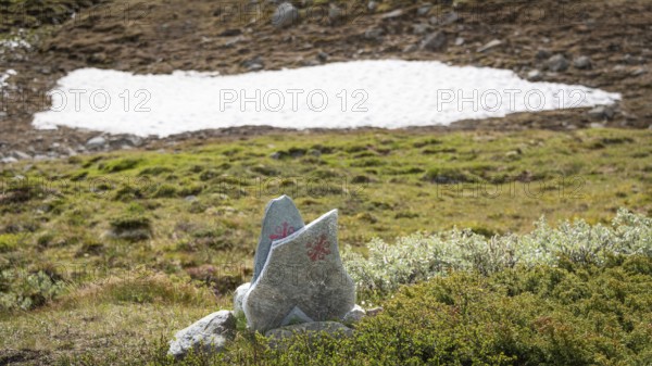 Olavskreuz auf Steinen, Wegmarkierung für Pilger, dahinter kleines Schneefeld in bergiger Landschaft, Pilgerweg Olavsweg, Olavsleden oder Pilgrimsleden, Dovrefjell, Norwegen