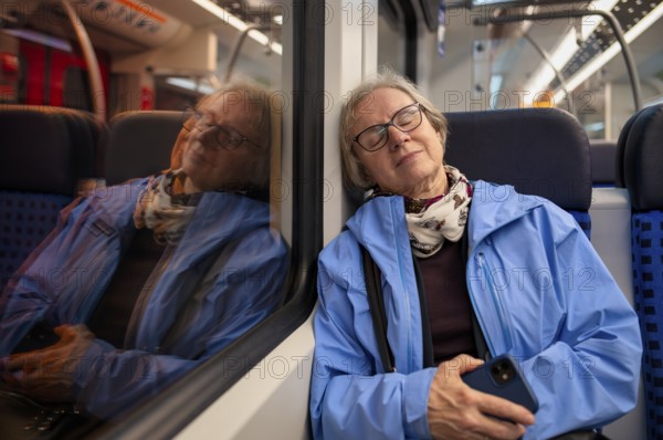 Innenaufnahme, ältere Frau, Brille, sitzt in S-Bahn, Zug, schläft, erschöpft, träumt, Smartphone, Handy, Spiegelung, abends, nachts, Nachtaufnahme, ÖPNV, Nahverkehr, Stuttgart, Baden-Württemberg, Deutschland