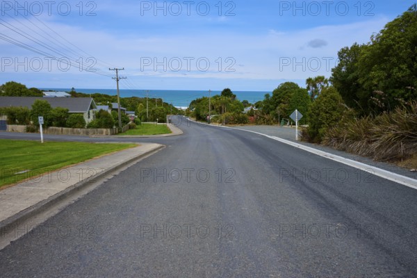 Küstenstraße mit Blick auf das Meer, gesäumt von ruhigen Häusern unter blauem Himmel, Kaka Point, Clutha District, Otago, Südinsel, Neuseeland