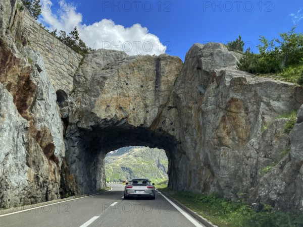 Porsche sports car drives through short rock tunnel Rock tunnel Tunnel on pass road from Alpine Pass to Susten Pass, Canton Uri, Switzerland