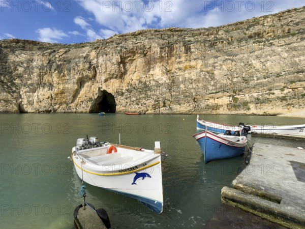 Moored excursion boat without tourists in inland sea of Gozo, in the background tunnel from passage through rock face to open sea, island of Gozo, Malta