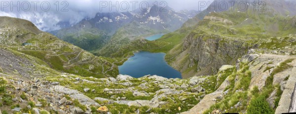 Panoramic view of left serpentine narrow bends from ascent pass road to Alpine pass Colle del Col de Nivolet, right foreground mountain lake Lago Agnel, rear reservoir Lago Serru Serrù, Gran Paradiso National Park, Ceresole Reale, Piedmont, Italy