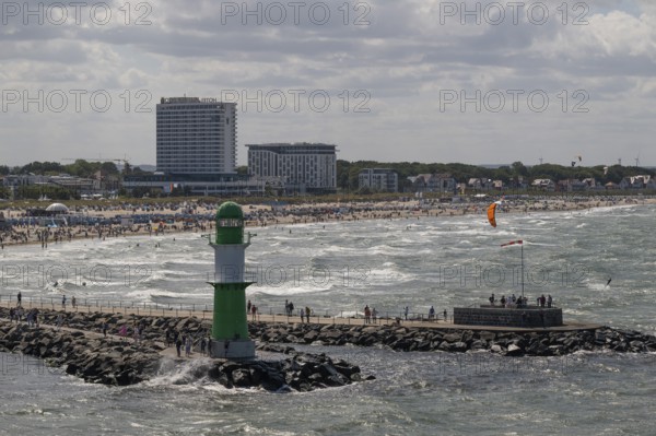 Green and white lighthouse, pier light Westmole in front of lively beach and hotels in the background, waves, Warnemünde, Rostock, Mecklenburg-Western Pomerania, Germany