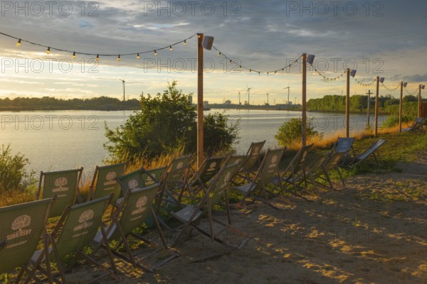 View from the outdoor area of a restaurant at Lankenauer Höft over deckchairs through a string of lights onto Neustadt harbour in the evening light, Weser, Bremen, Germany
