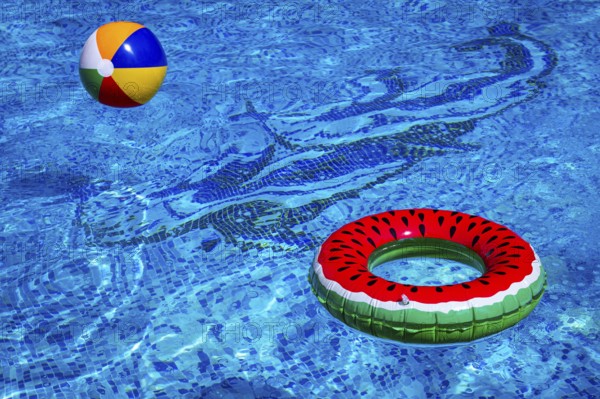 Colorful beach ball and watermelon circle, floating in the pool water, on a sunny summer day, no people