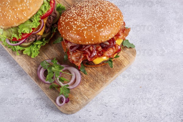 Two burgers with beef patty, fried bacon, cheddar cheese, tomatoes, homemade, no people