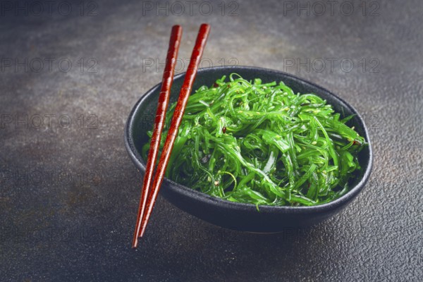 Chuka salad, made from fresh seaweed, with sesame dressing, served in a black bowl, with chopsticks