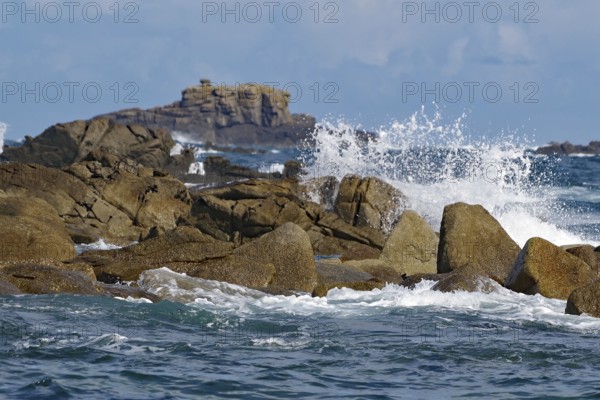 Waves crashing against rocks with a rocky background under a blue sky, Isles of Scilly, Cornwall, Great Britain
