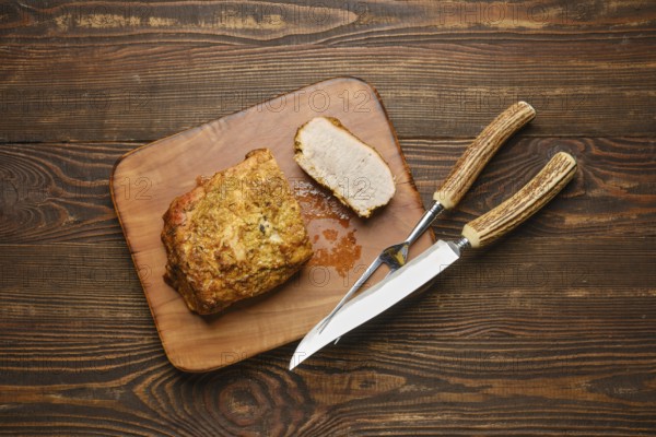 A deliciously roasted piece of pork meat on a wooden cutting board served with carving knife and fork