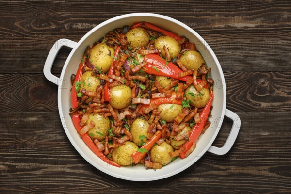 Golden baby potatoes are roasted with vibrant red peppers and crispy bacon on wooden background