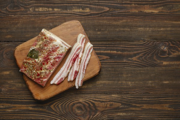 Thick slices of seasoned bacon on a wooden cutting board, showcasing a blend of herbs and spices