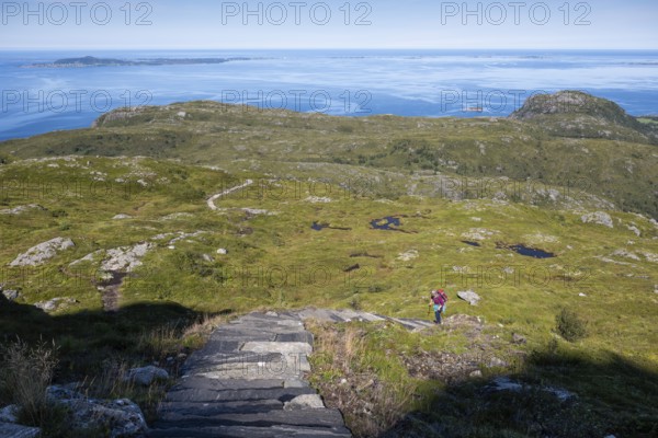 Woman with backpack climbing up stone stairs, Sherpat stairs or Midsund stairs or Midsundtrappene, Bløkallen hike, in the background sea and islands, island Otroya or Otrøya, Møre og Romsdal, Norway