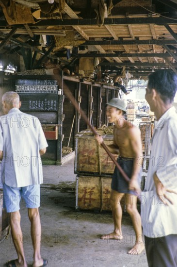 Workers having fun at store ice building at the fish market, East coast, Mersing, Johor, Malaya, Malaysia, south east Asia 1964
