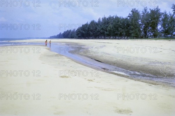 Men walking on sandy beach south of estuary, Rompin, East coast, Pahang, Malaya, Malaysia, south east Asia 1964