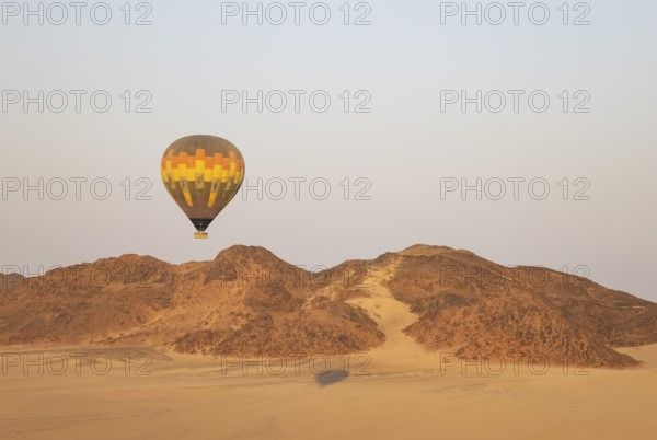 The hot-air balloon above an arid plain and isolated mountain ridges at the edge of the Namib Desert. Aerial view from a second balloon. Namibia