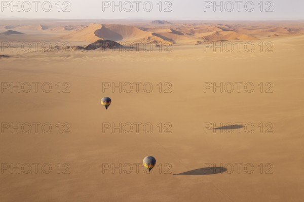 Two hot-air balloons above an arid plain at the edge of the Namib Desert. Aerial view from another balloon. Namibia