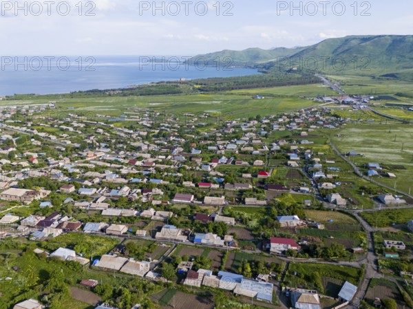 Vast landscape with houses and green fields by the sea and mountains in the distance, aerial view, Tsovagyugh, Lake Sevan, Gegharkunik Province, Armenia