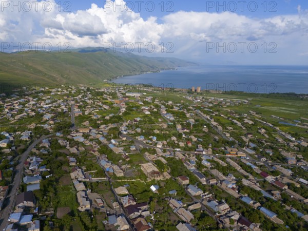Town with densely packed houses and a view of the sea and mountains under a cloudy sky, aerial view, Tsovagyugh, Lake Sevan, Gegharkunik Province, Armenia