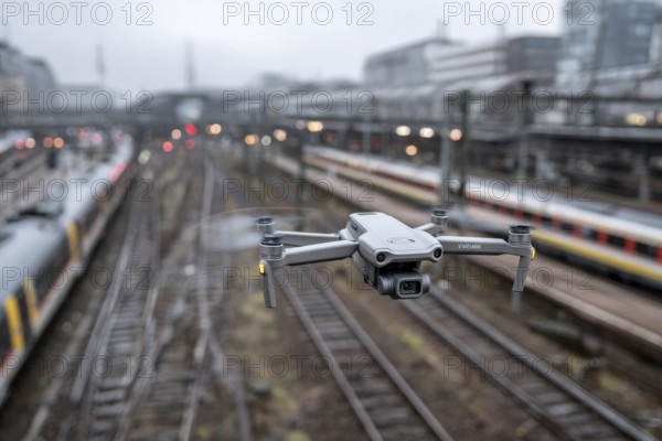 Ein Fernpilot steuert sein Quadrocopter, Drohne illegal über Bahnhofsgelände, Bahngelände, Bahnschienen, Symbolbild für illegaler Drohnenbetrieb über Bahnanlagen, kritische Infrastruktur, Kontrollierter Luftraum, Flugverbot, Betriebsverbot, gefährlicher Eingriff in den Bahnverkehr, AI generiert, AI generated