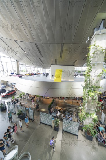View from above of a modern room with plants and people under a yellow accent, BMW Welt, Munich, Germany