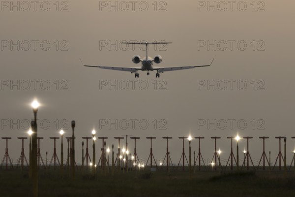 Executive business jet passenger aircraft landing over runway lights at sunset, London Stansted airport, Essex, England, United Kingdom