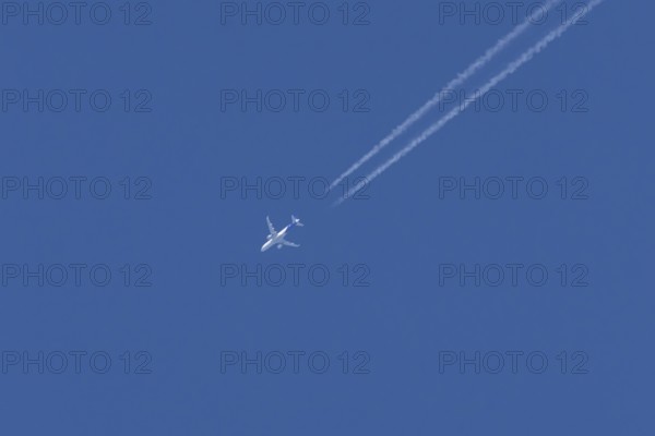 Jet passenger aircraft with a vapour trail or contrail flying in a blue sky, England, United Kingdom