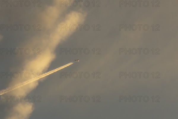 Jet passenger aircraft with a vapour trail or contrail flying in a sky with clouds, England, United Kingdom