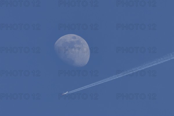 Boeing 737 jet passenger aircraft of Norweign Air with a vapour trial or contrail behind flying in a blue sky passing by the moon, England, United Kingdom