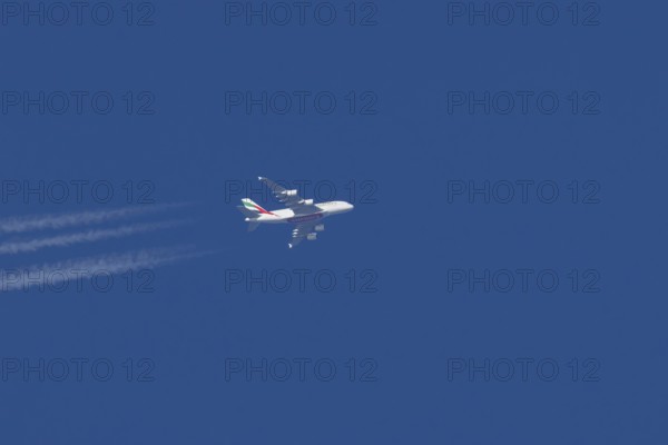 Airbus A380 jet passenger aircraft of Emirates airlines with a vapour trail or contrail flying in a blue sky, England, United Kingdom