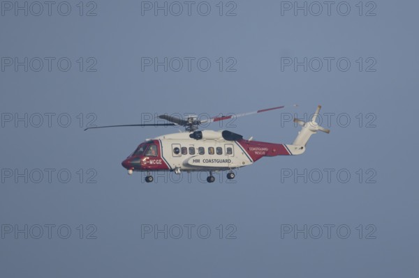Sikorsky S-92A helicopter of the UK HM Coastguard flying in a blue sky, England, United Kingdom