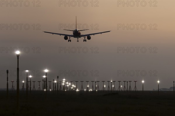 Jet passenger aircraft landing over runway lights at sunset, London Stansted airport, Essex, England, United Kingdom