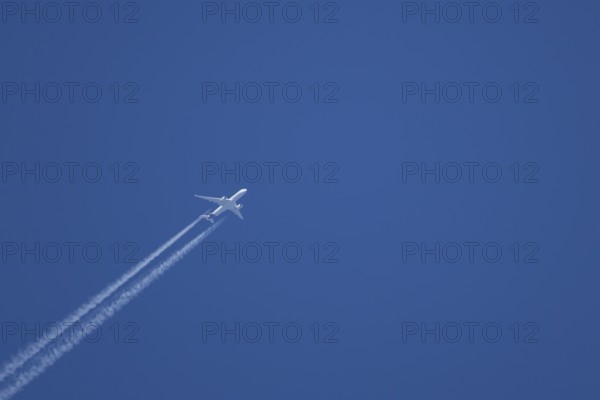 Jet passenger aircraft with a vapour trail or contrail flying in a blue sky, England, United Kingdom