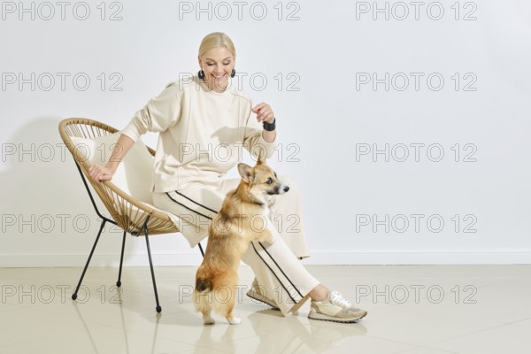 A joyful woman in a light outfit interacts with her playful corgi in a stylish indoor space. The cozy atmosphere highlights their bond, showcasing a moment of happiness and companionship