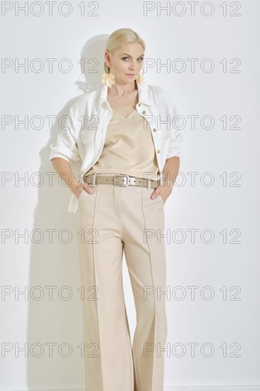 A model showcases a chic outfit featuring a light-colored top and tailored trousers, complemented by a buttoned jacket