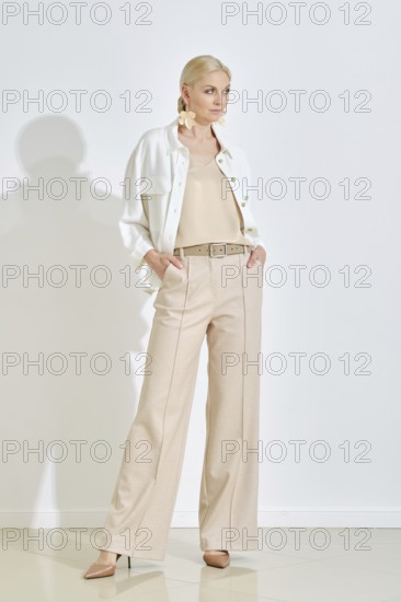 A woman stands confidently wearing a light-colored outfit that includes wide-leg trousers and a stylish jacket