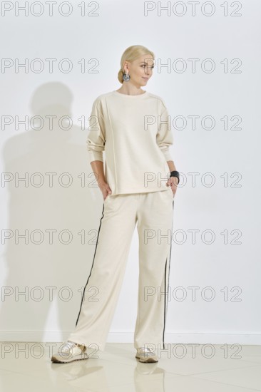 Model poses confidently in a neutral-toned outfit, featuring a sweatshirt and wide-leg pants. Soft lighting from large windows enhances the relaxed vibe of this minimalist studio setting