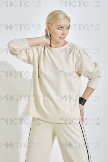 A woman showcases a light-toned casual outfit featuring a relaxed sweatshirt and stylish pants. She strikes a confident pose, highlighting her accessories against a clean white backdrop