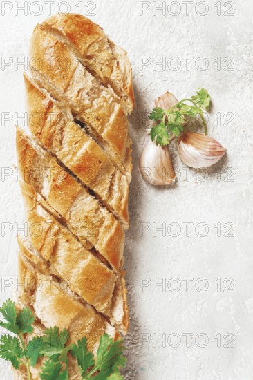 Garlic bread, baguette with garlic butter and herbs, on a light table, top view