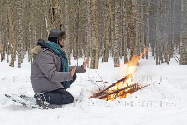 A woman warms herself by a campfire in winter, Gaspesie national park, Province of Quebec, Canada, north America