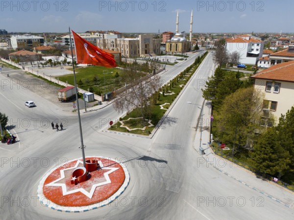 Roundabout with large red flag in urban environment, surrounded by streets and parks, aerial view, Sultanhani, Sultanhani Kervansaray, Aksaray province, historic Silk Road, Turkey