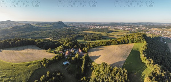 Luftbild, Panorama von einer vulkanisch geprägten Landschaft im Abendlicht, im Vordergrund der Phonolithkegel Rosenegg, am Horizont die Hegauberge mit dem Hohentwiel und der Stadt Singen mit der angrenzenden Gemeinde Rielasingen-Worblingen, Hegau, Landkreis Konstanz, Baden-Württemberg, Deutschland