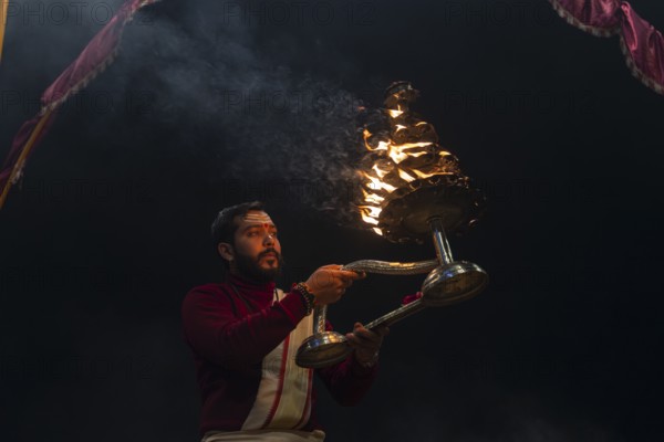 Hindu priest performing the Aarti ritual, holding a burning oil lamp, at the Ganges, Bangali Tola, Varanasi, Uttar Pradesh, India