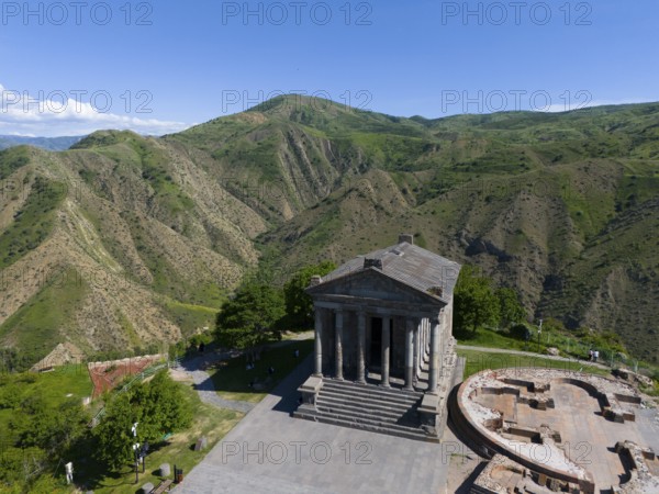 An ancient temple stands against a green mountain backdrop under a blue sky, aerial view, Temple of Garni, Garni, Kotayk province, Armenia