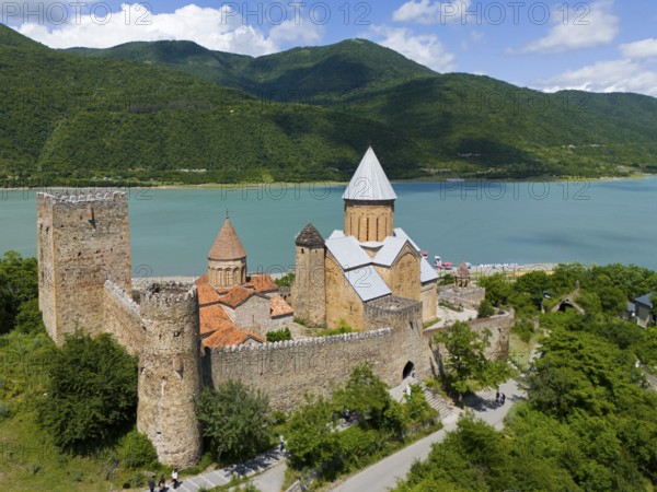 Medieval castle on the lake in front of forested mountains with peaceful atmosphere under blue sky, aerial view, Ananuri castle, Zhinvali reservoir, Shinvali, Jinvali or Shinvali, Mtskheta-Mtianeti region, Georgian Military Road, Georgia
