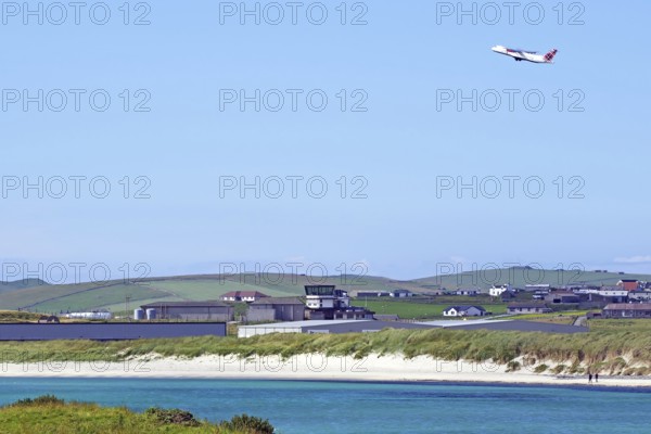 Aeroplane taking off over coast with hangars and green land, Sumburgh Head, Shetland Islands, Scotland, United Kingdom
