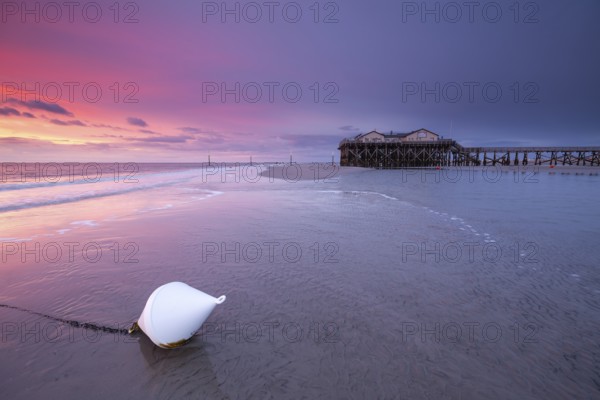 Pile dwellings in St. Peter-Ording in front of the surf in the bright red evening light by the sea