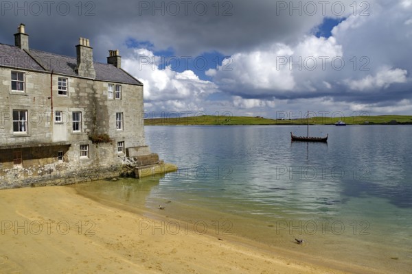 Old stone cottage on quiet loch shore with sandy beach and passing boat under cloudy sky, Murder in Shetland crime series, Viking ship, Up Helly A, Lerwick, Shetland Islands, Scotland, United Kingdom