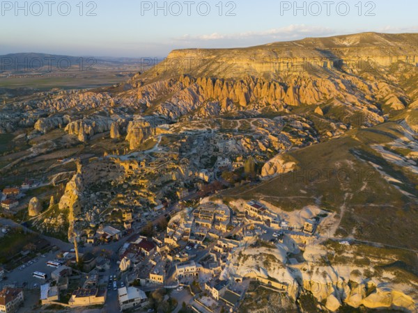 Stone formation at sunset over a village with a golden skyscape, aerial view, Göreme National Park, Göreme Tarihî Millî Parki, Nevsehir Province, Nevsehir, Cappadocia, Cappadocia, Cappadocia, Cappadocia, Central Anatolia, Turkey